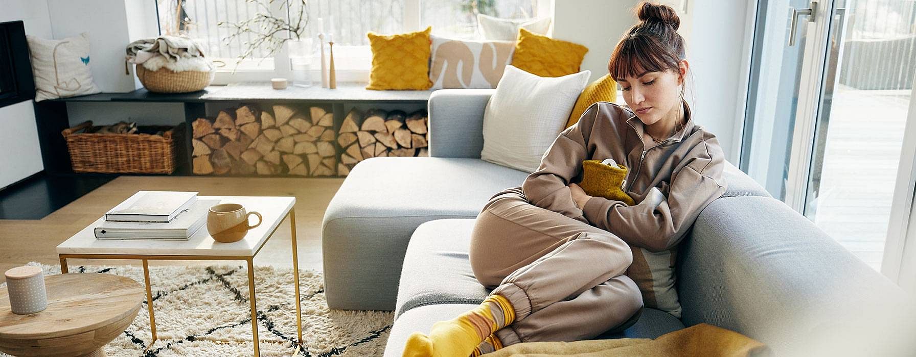 Frau mit Wärmeflasche auf dem Sofa im Wohnzimmer