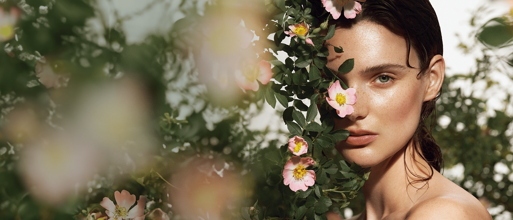 Portrait d'une jeune femme qui se cache derrière un buisson de roses sauvages