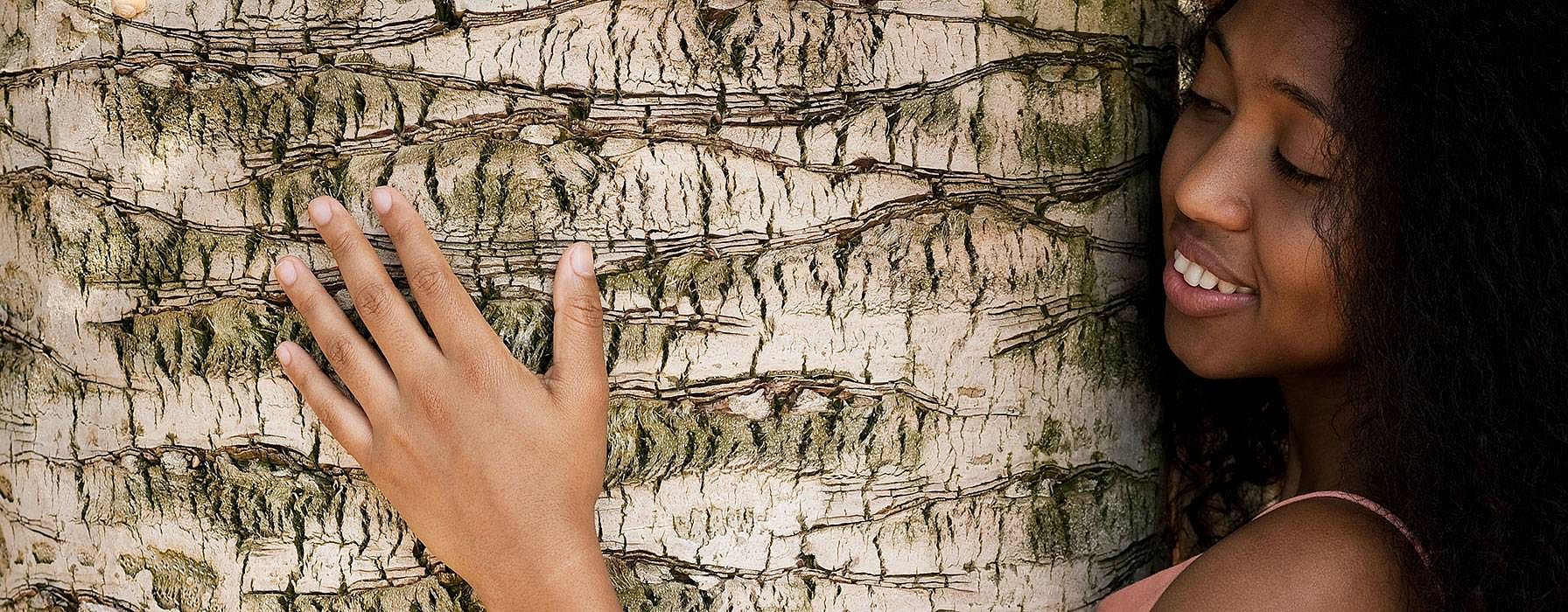 Jeune femme touche tronc d'un arbre