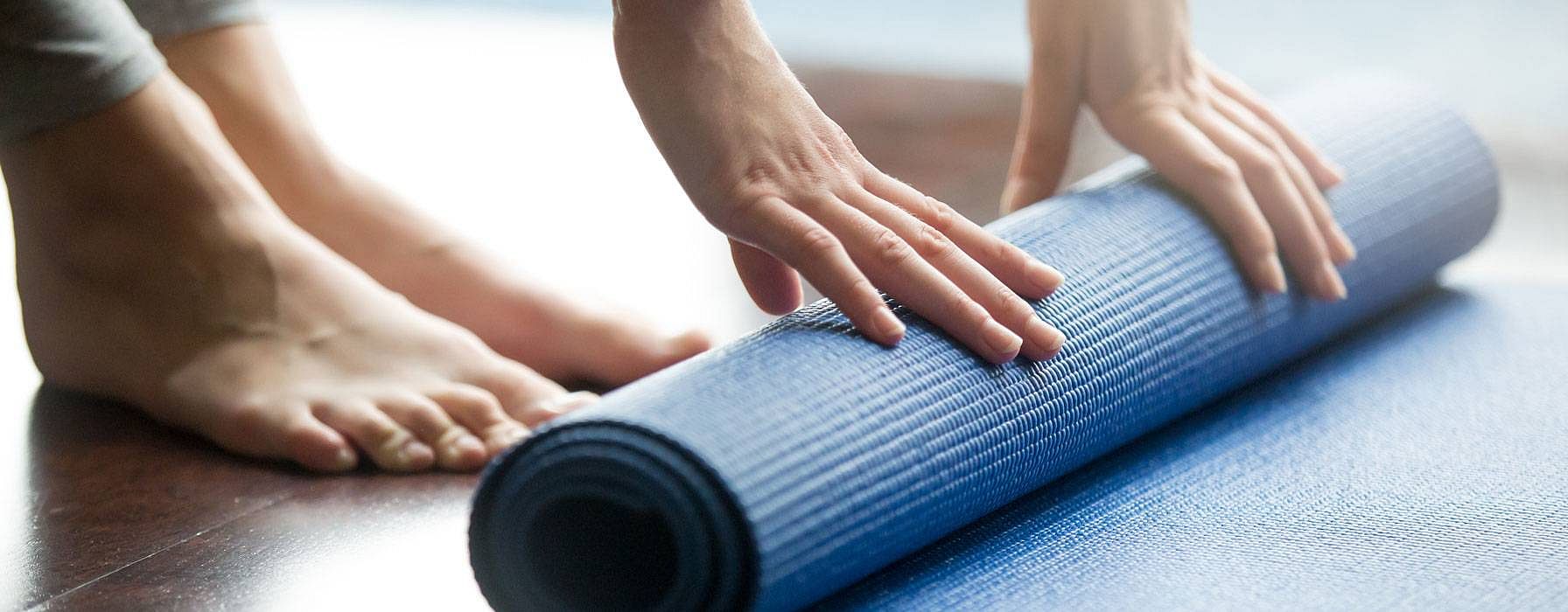 Eine Frau rollt einen Yogateppich zusammen