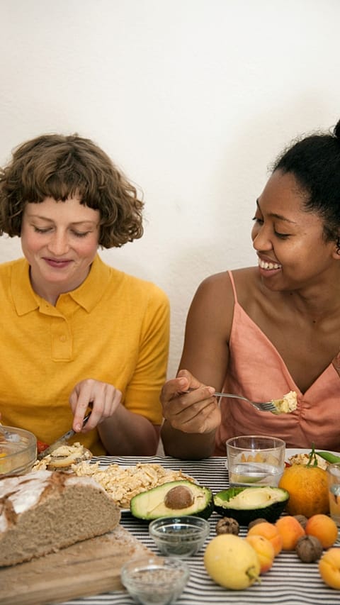 Deux femmes mangent des fruits, de l'avocat, du pain complet, des flocons d'avoine, des graines, des noix