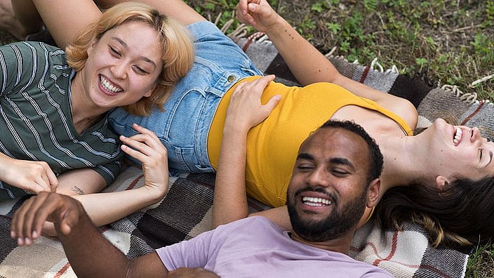 Trois amis rient sur une couverture dans l'herbe