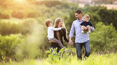 Un homme et une femme se promènent dans la nature en se tenant la main, chacun avec un enfant dans les bras.