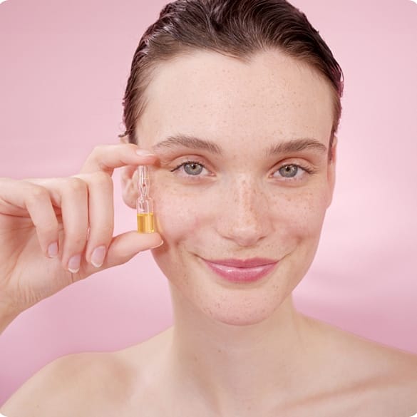 Une jeune femme tient le sérum réparateur pour la peau à la Rose musquée Weleda contre sa joue.