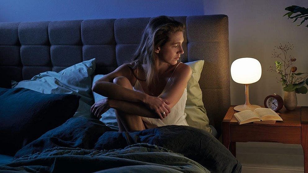 Femme au lit dans une chambre sombre avec une lampe de chevet allumée