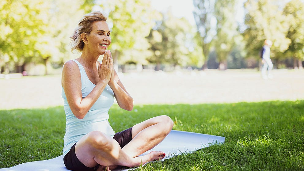 Une femme âgée fait du yoga dans le parc.