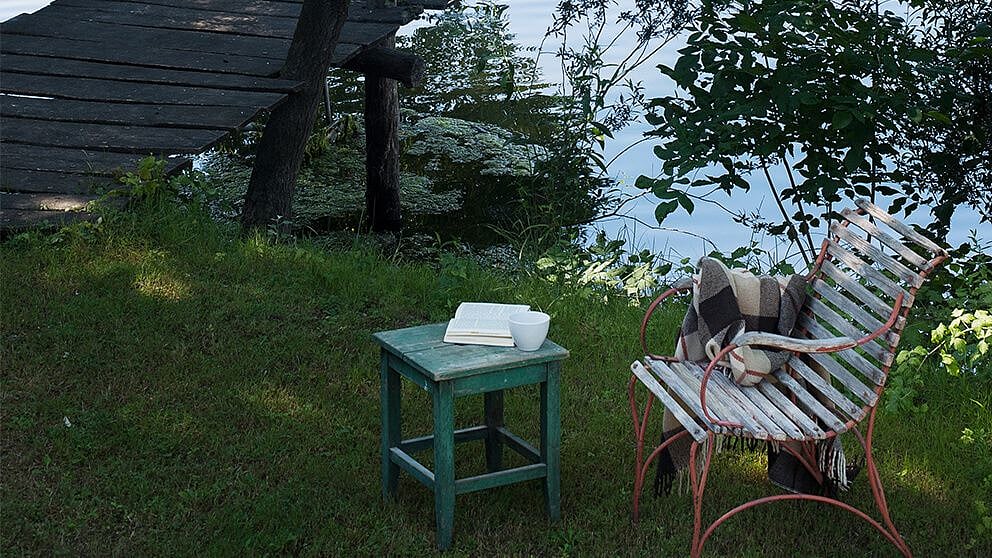 chaise dans la nature avec couverture au bord de l'eau et ponton avec petite table et thé
